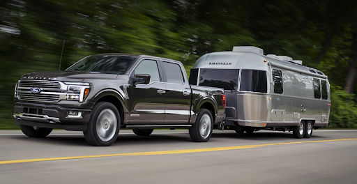 A black Ford F-150 pickup truck tows a silver Airstream trailer down the road as trees whizz past.