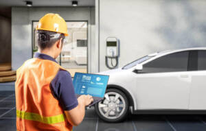 man in orange vest holding a laptop by a white car