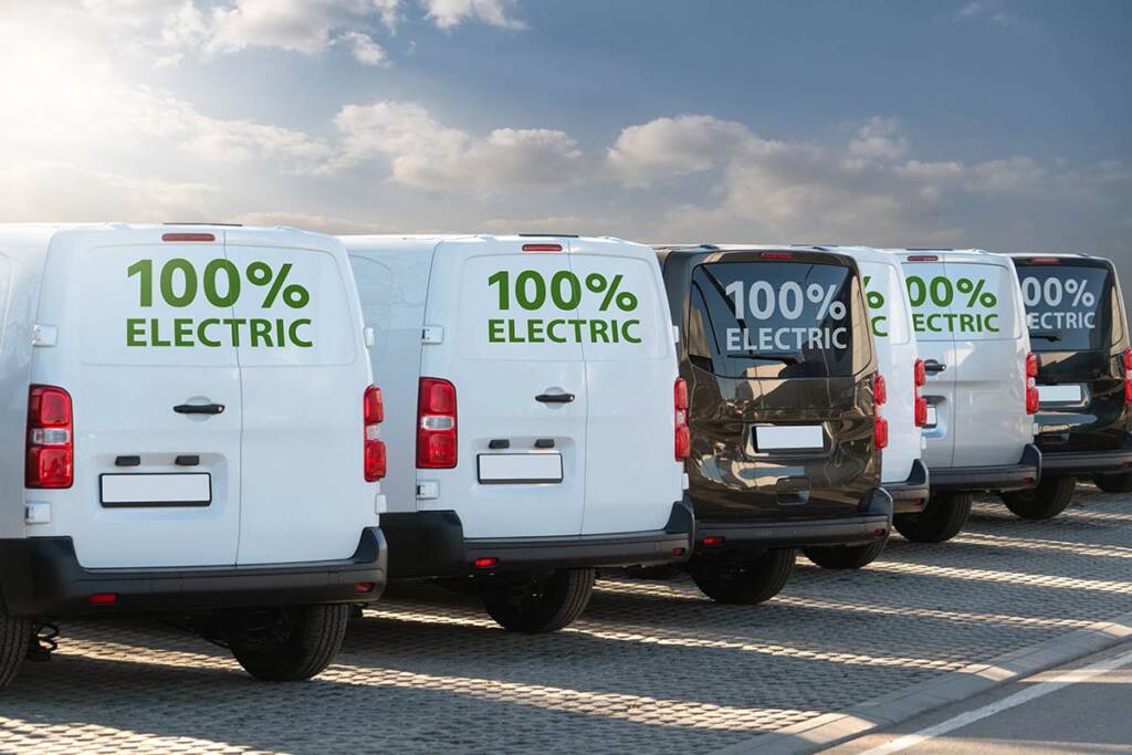 Fleet of five electric vans parked in a row, each displaying "100% Electric" on their rear windows.