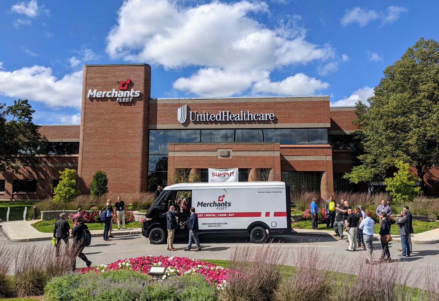 A Merchants Fleet van and people are in front of a UnitedHealthcare building on a sunny day.
