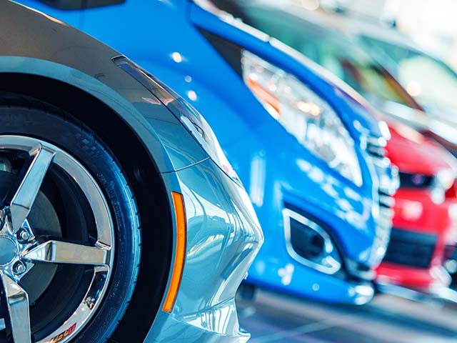 Close-up of a row of parked cars in various colors, with a focus on a silver car's wheel.