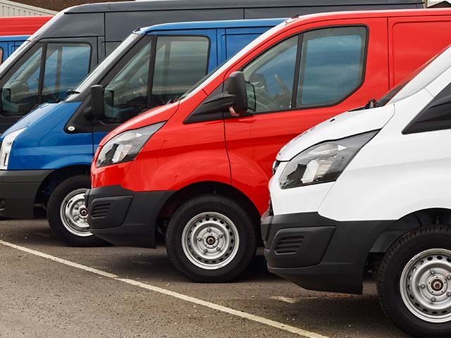 A row of parked vans in blue, red, and white on an asphalt surface.