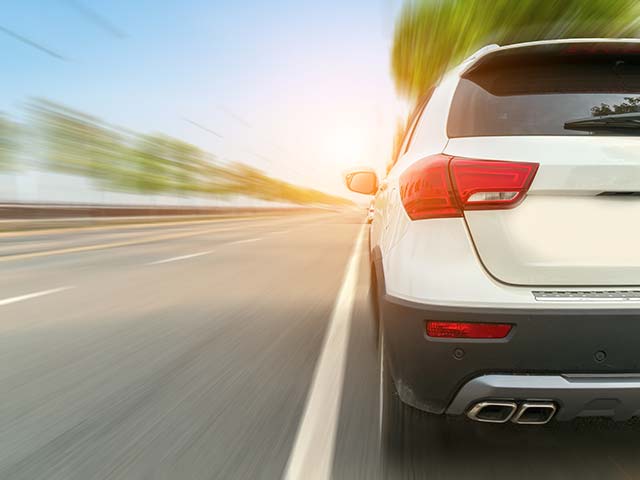 White SUV driving fast on a sunny road with a motion blur effect.