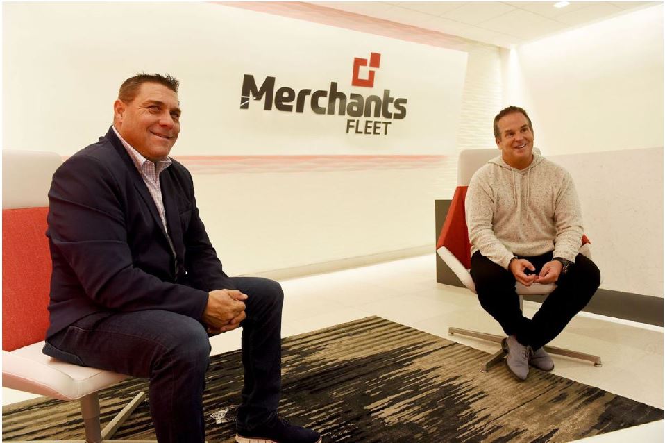 Two people sitting in a modern office lobby with a "Merchants Fleet" sign on the wall behind them.