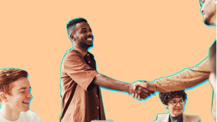 Four people in a meeting room, two are shaking hands, smiling, against an orange backdrop.