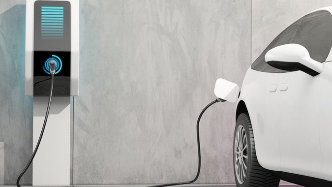 Electric car charging at a charging station against a gray wall.