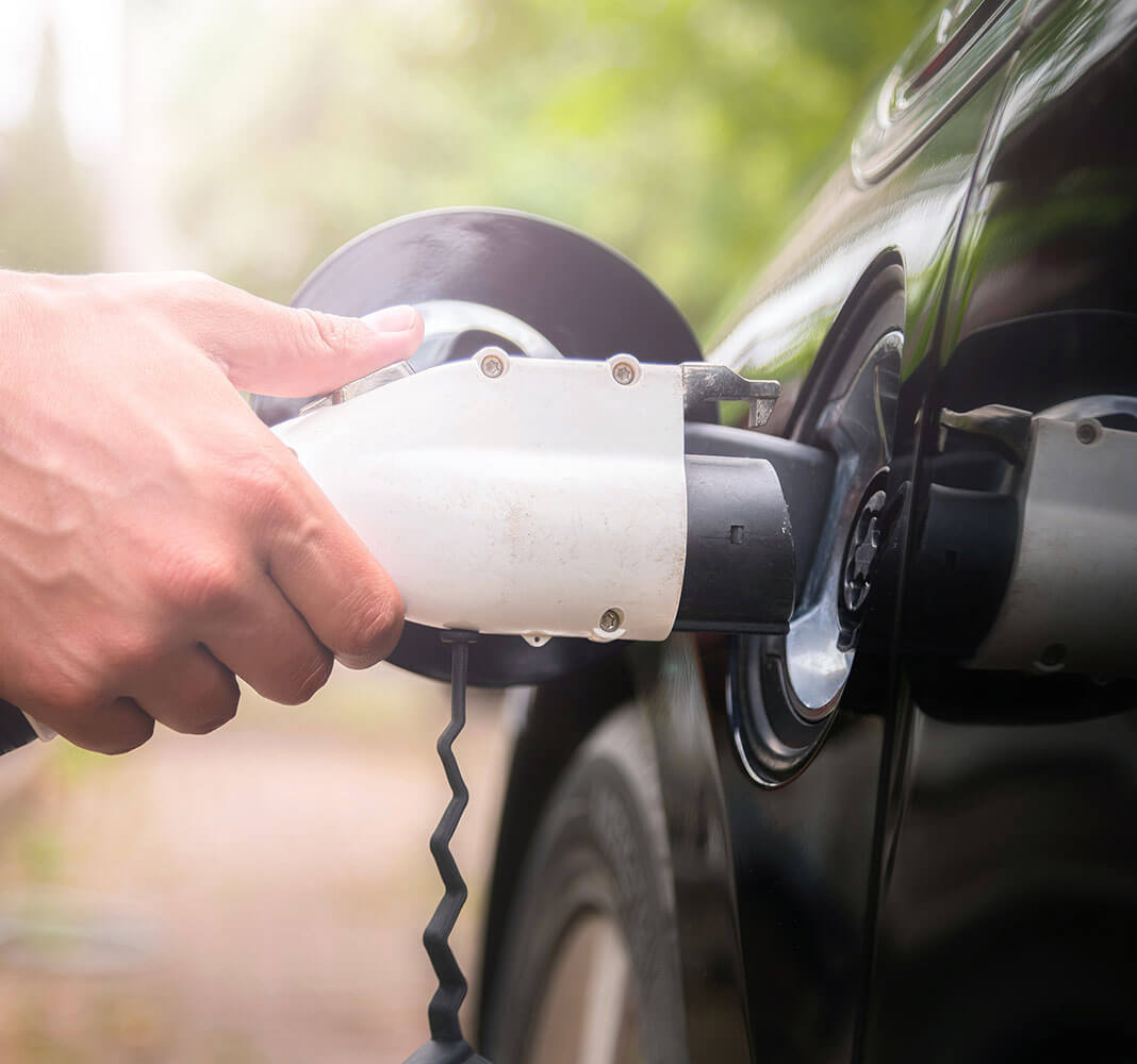 Close-up of a hand inserting an electric vehicle charger into a black car's charging port.