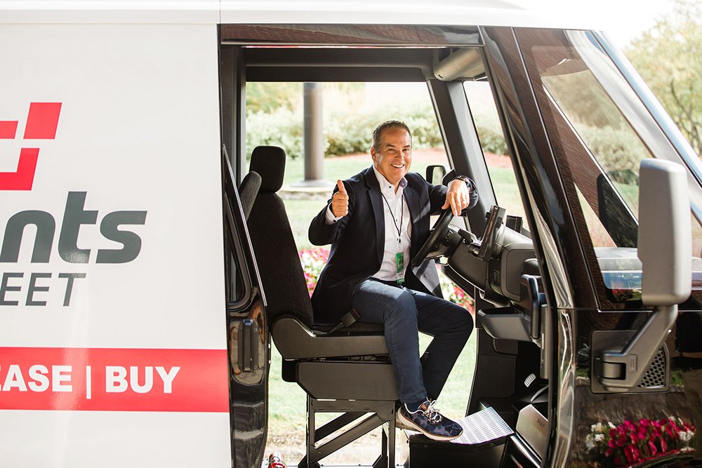 Man sitting and giving a thumbs-up in the driver's seat of a parked van with "Lease | Buy" written on the side.