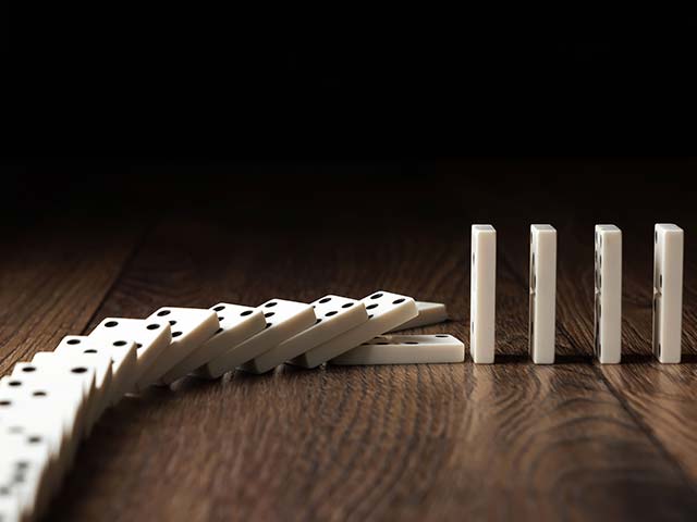 Dominoes falling in a line on a wooden surface with one domino yet to topple.