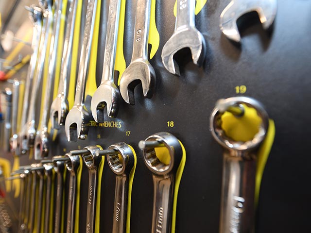 Close-up of various wrenches hanging on a black wall, organized by size with yellow numbered labels.