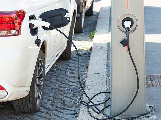Electric car charging at a street charging station with cables connected.