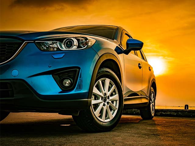 Blue car parked with a golden sunset in the background.