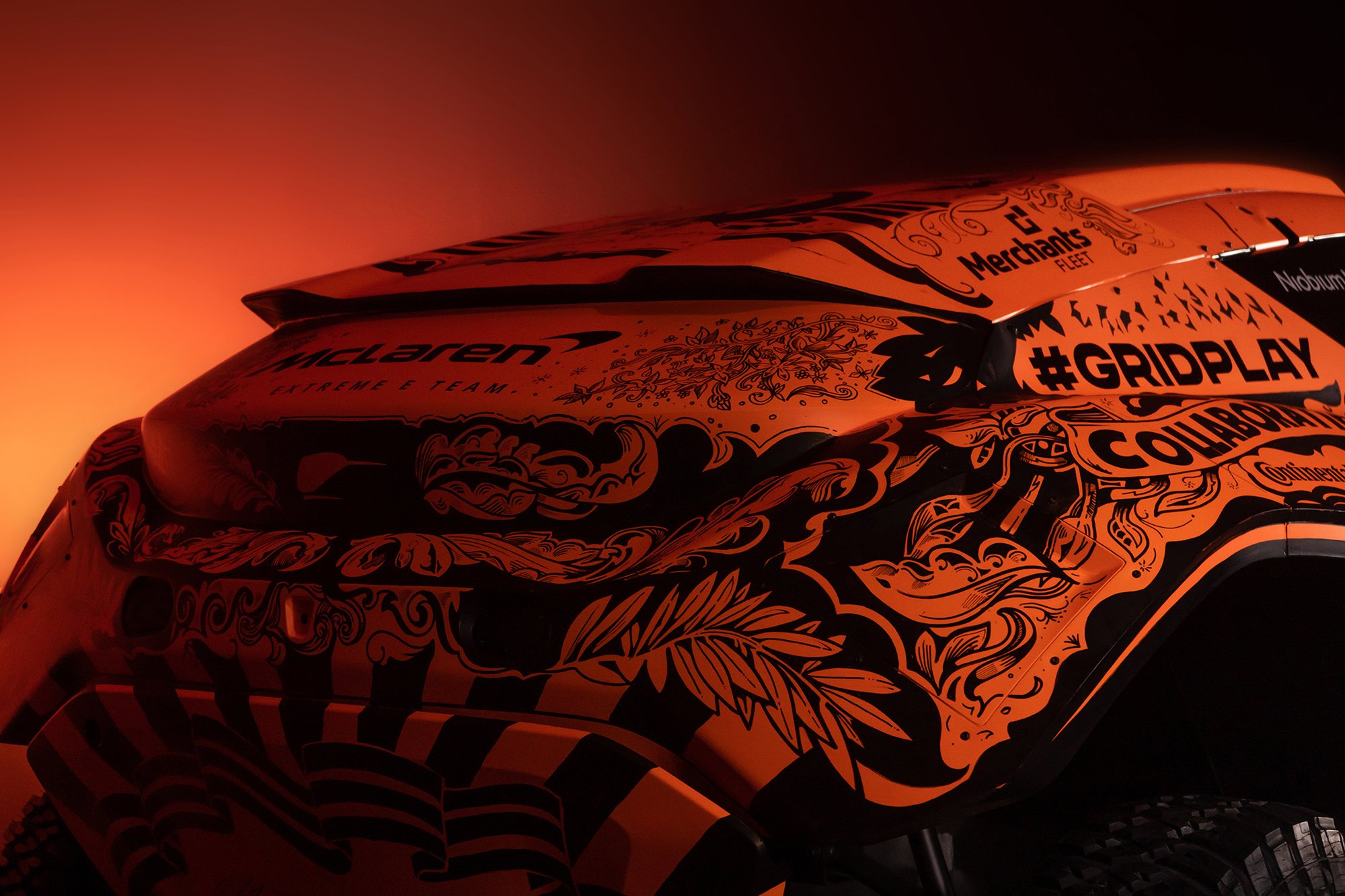 Close-up of an orange race car with intricate black designs and decals, set against a warm, glowing background.