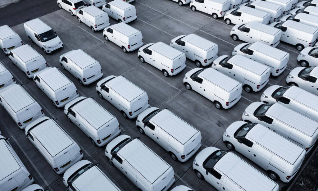 Aerial view of numerous white vans parked neatly in a large parking lot.