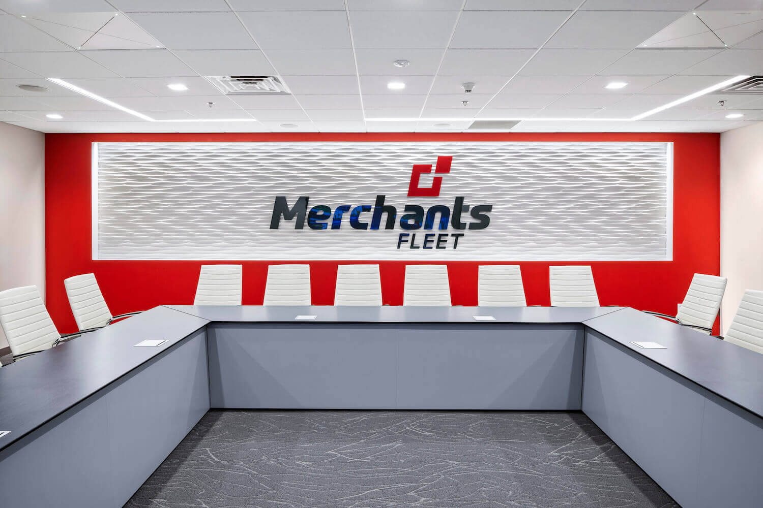 Conference room with a long table, white chairs, and a "Merchants Fleet" logo on a red and white wall.