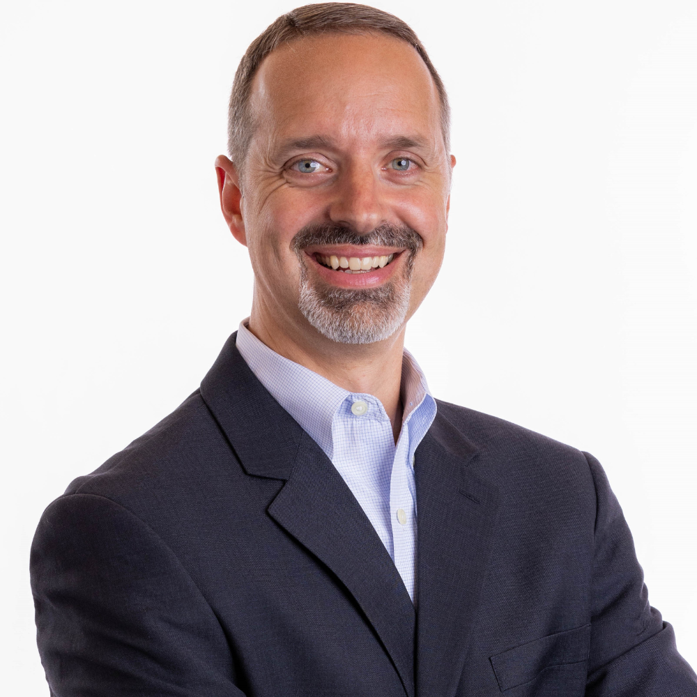 Smiling person in a suit with crossed arms against a white background.