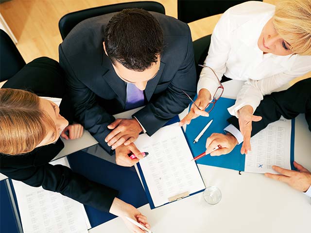 Overhead view of four people in formal attire discussing documents at a table.