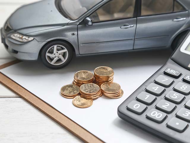 Toy car, stacked coins, and calculator on paper, symbolizing car expenses or budgeting.