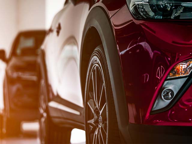 Close-up of the front wheels and headlights of two parked cars in a showroom, with a focus on the red car.