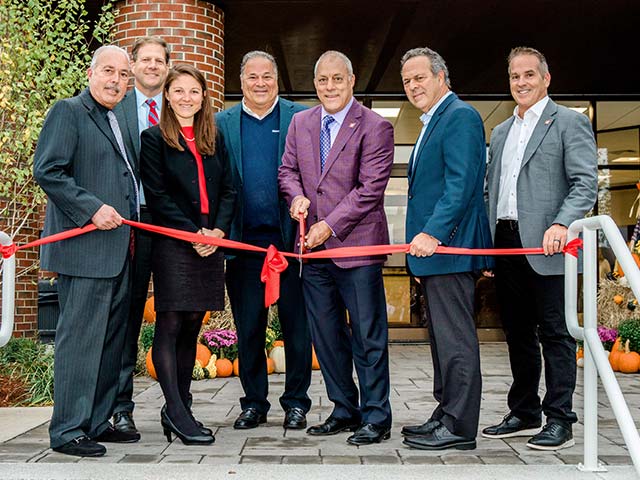 Group of people smiling at a ribbon-cutting ceremony in front of a building entrance.