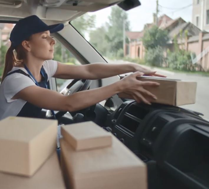 Delivery person organizing parcels on the dashboard of a vehicle on a residential street.