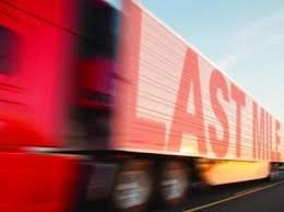 Red truck with "LAST MILE" on its side, moving quickly on a road, with a clear sky in the background.