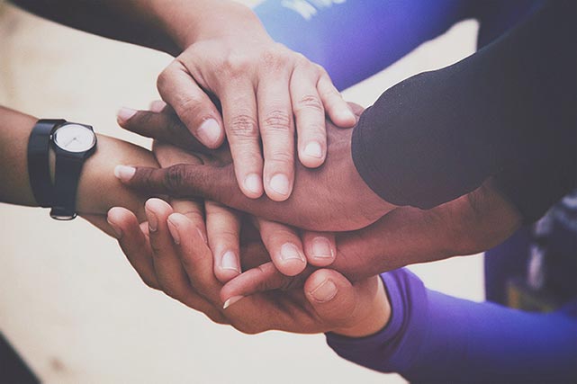 Stacks of diverse hands placed on top of each other symbolizing unity and teamwork.