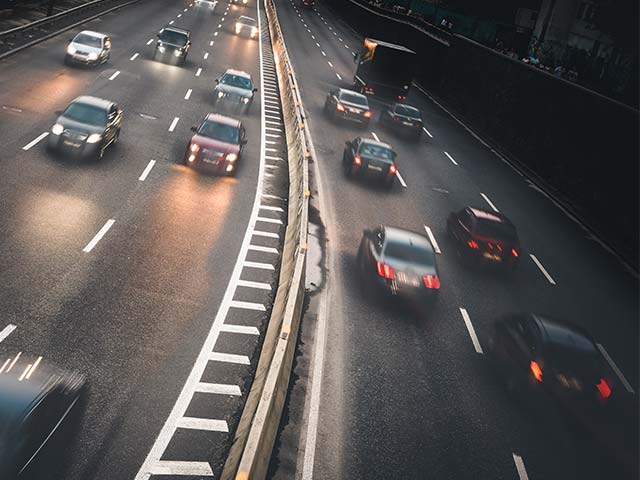 Traffic on a busy highway with cars moving in both directions, separated by a concrete barrier.