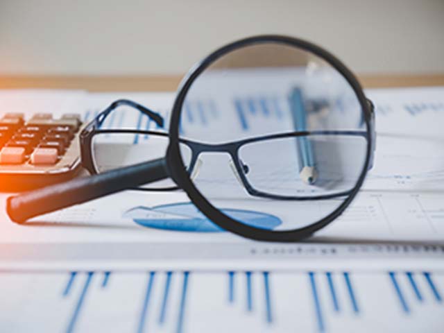 Magnifying glass and glasses on financial charts, next to a calculator and pen.