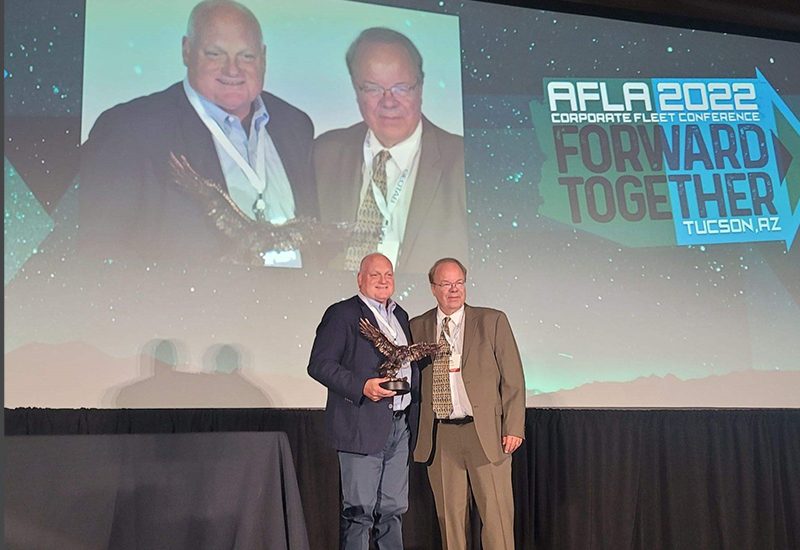 Two men on stage at AFLA 2022 in Tucson, AZ; one holds an award, and a large screen displays their photo.