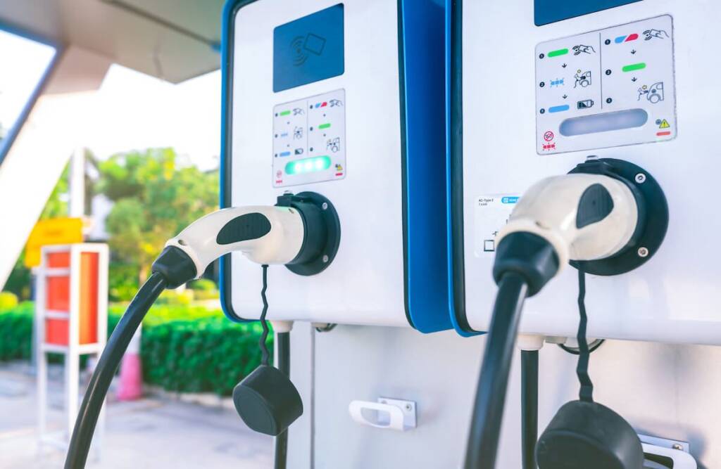 Two electric vehicle charging stations with plugged-in cables at an outdoor charging point.