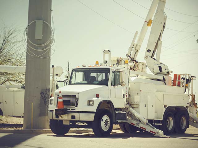 Utility truck parked by a power pole, equipped with a cherry picker and cones in an outdoor setting.
