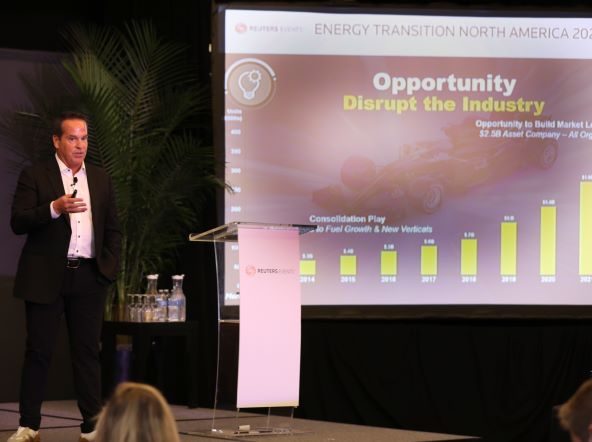 Man speaking at a podium next to a projection screen displaying a graph and text about industry opportunities.