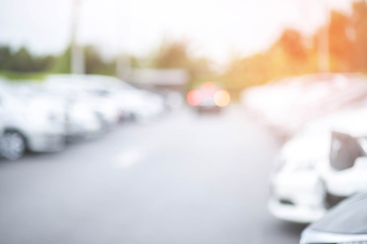 Blurred image of parked cars on a street with a distant car driving away, under soft sunlight.