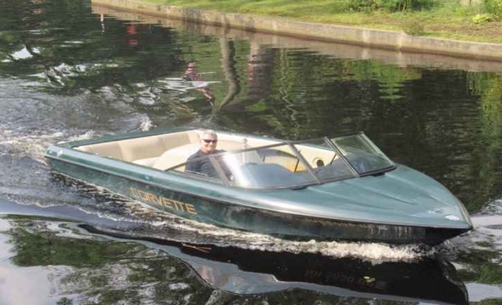 Person steering a sleek, dark-colored speedboat named Turvette on a calm canal.