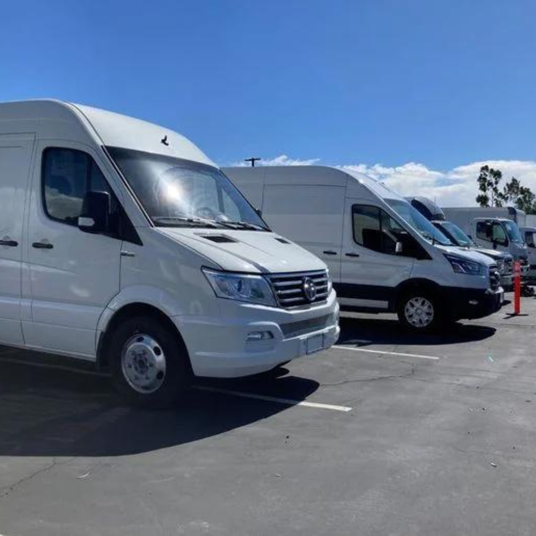 Several white delivery vans parked in a sunny lot under a clear blue sky.