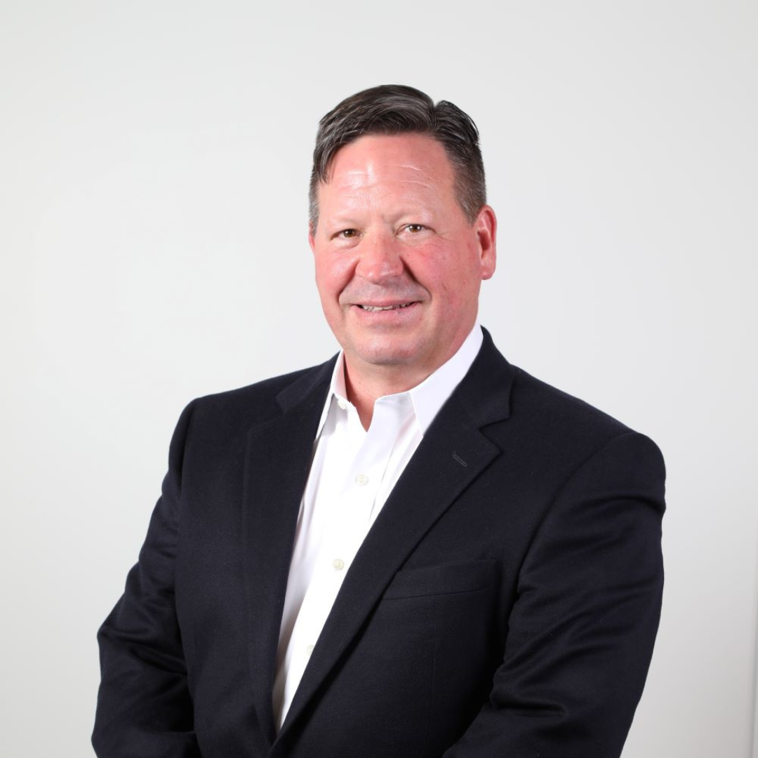 Man in a black suit and white shirt smiling against a plain white background.