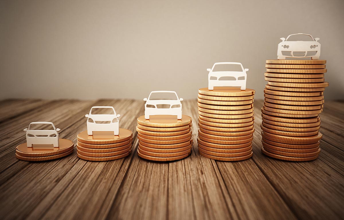 Stacks of coins with car silhouettes on top, arranged in ascending order on a wooden surface.