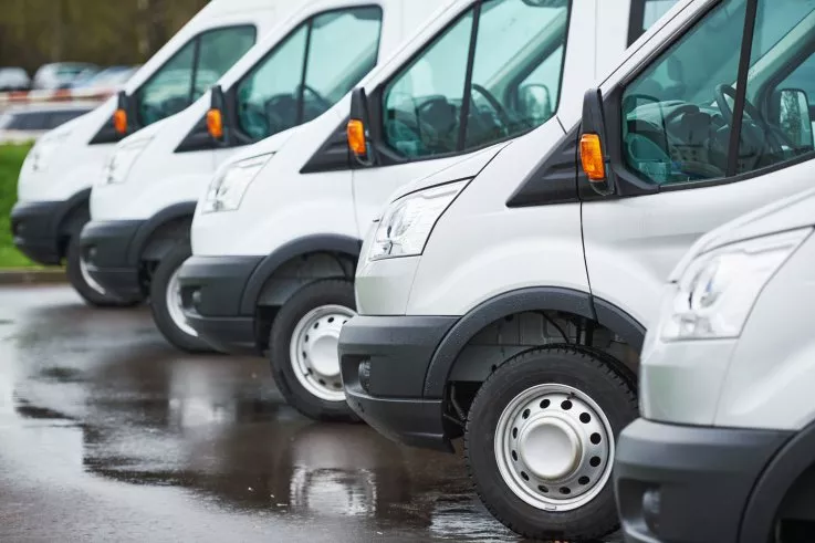Row of white delivery vans parked on wet pavement, viewed from the side.