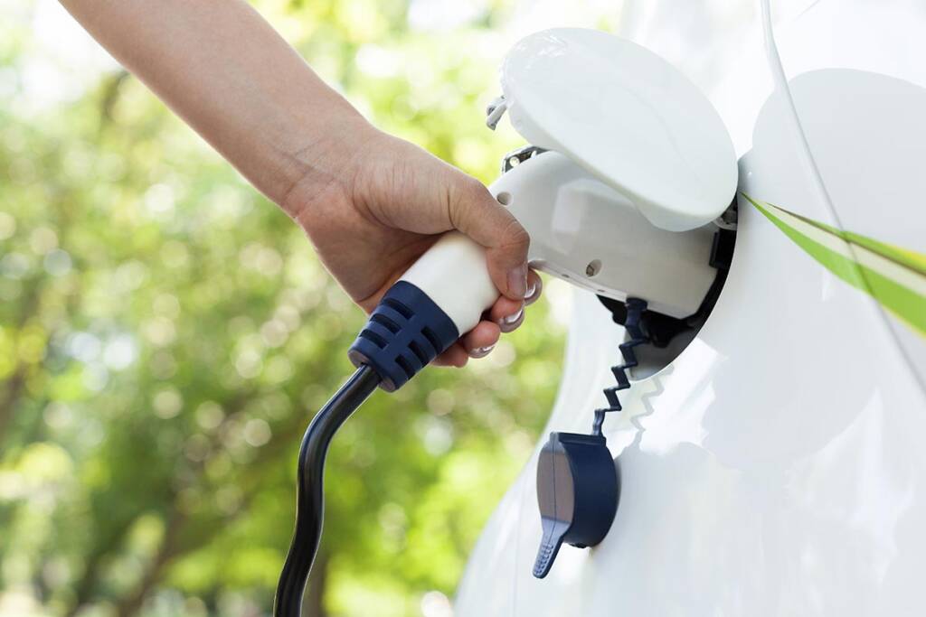 A person's hand plugging a charging cable into a white electric car.