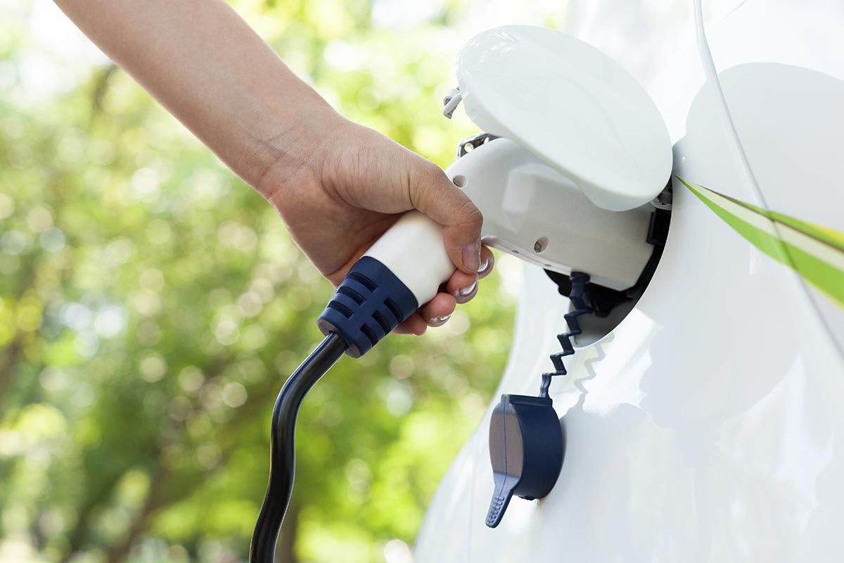 A person's hand plugging a charging cable into a white electric car.