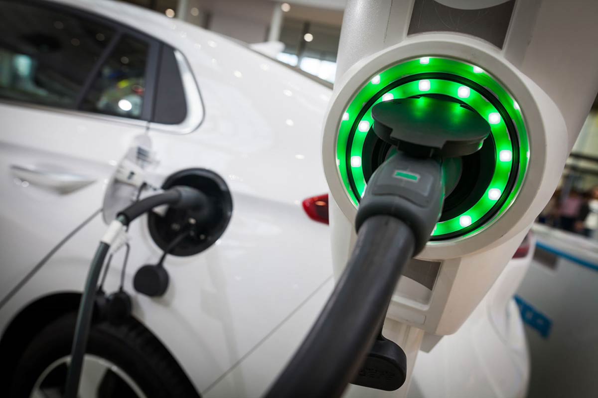 Close-up of an electric vehicle plugged into a charging station, with a green light indicating charging status.