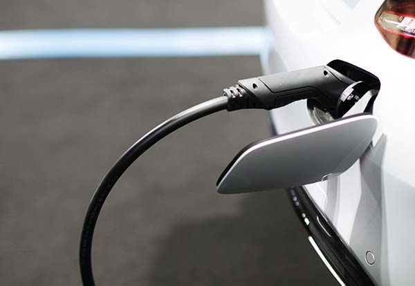 Electric car charging with a black cable connected to the port, showing partial view of the vehicle.