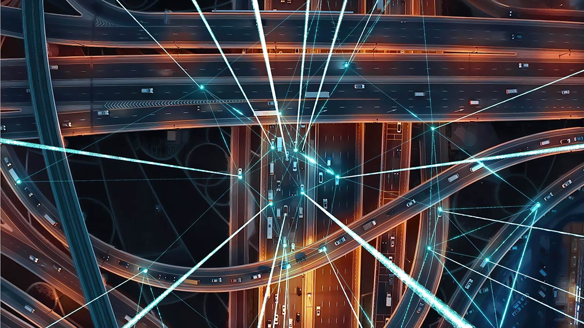 Aerial view of a busy highway interchange at night, with light trails from moving vehicles forming bright lines.