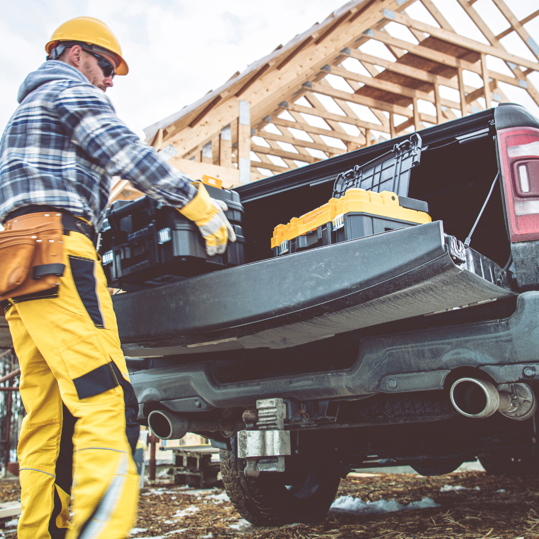 Construction worker unloading tools from a truck at a building site.