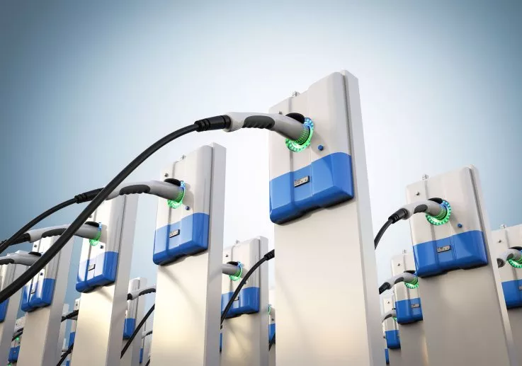 Multiple electric vehicle charging stations with cables and blue accents against a clear sky.
