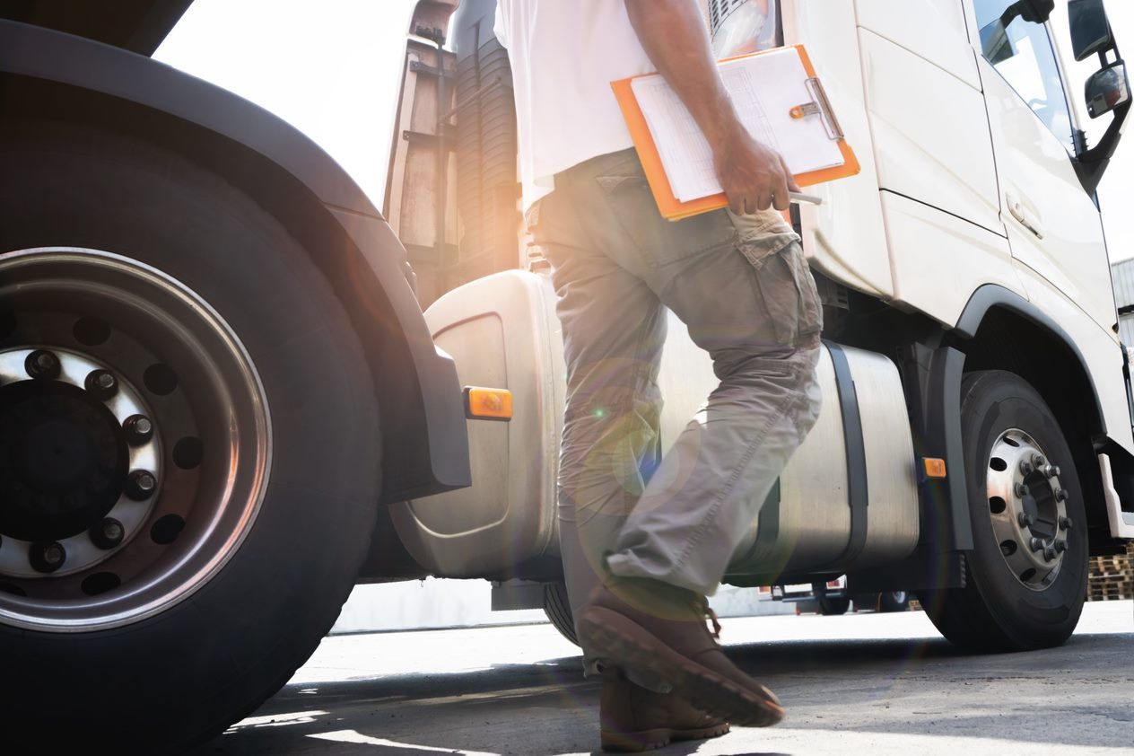 Person holding clipboard walking beside a parked truck, with sunlight creating lens flare in the background.