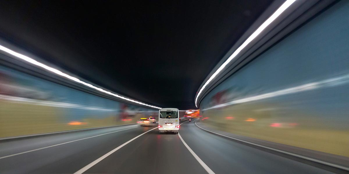 A bus driving through a brightly lit tunnel at night with blurred motion effects.