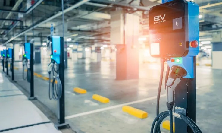 Electric vehicle charging stations in a parking garage with bright overhead lighting.