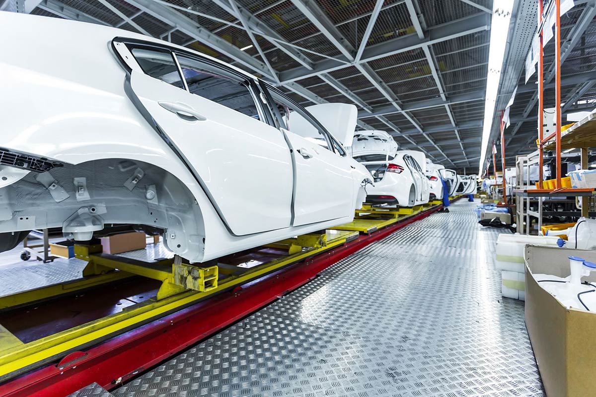 Assembly line with white car bodies on a factory floor, under bright lighting.